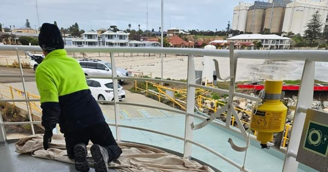 Employee in high vis painting boat railings during repairs and maintenance.